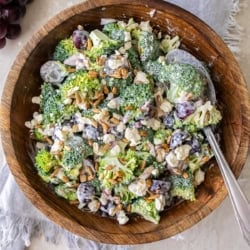A serving spoon resting in a wood bowl filled with broccoli grape salad.