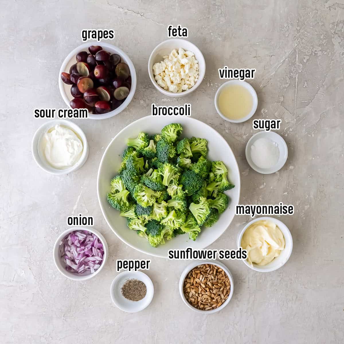 Broccoli florets, dried cranberries, feta, grapes and other ingredients in bowls with text overlay.
