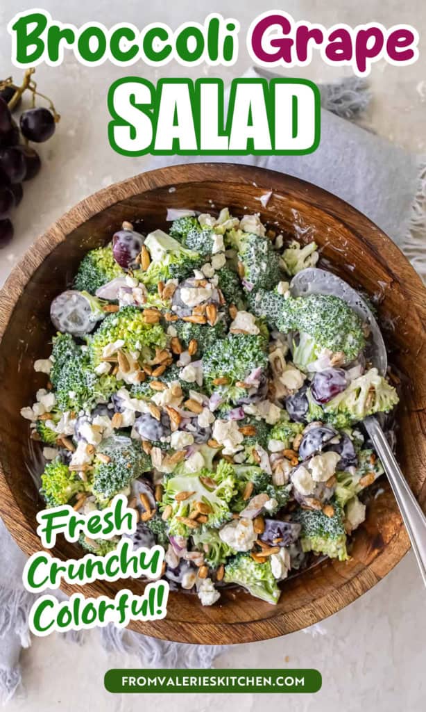 A serving spoon resting in a wood bowl filled with broccoli grape salad with text overlay.