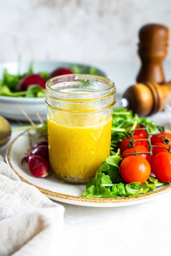 A mason jar filled with champagne vinaigrette on a plate with salad greens and cherry tomatoes.