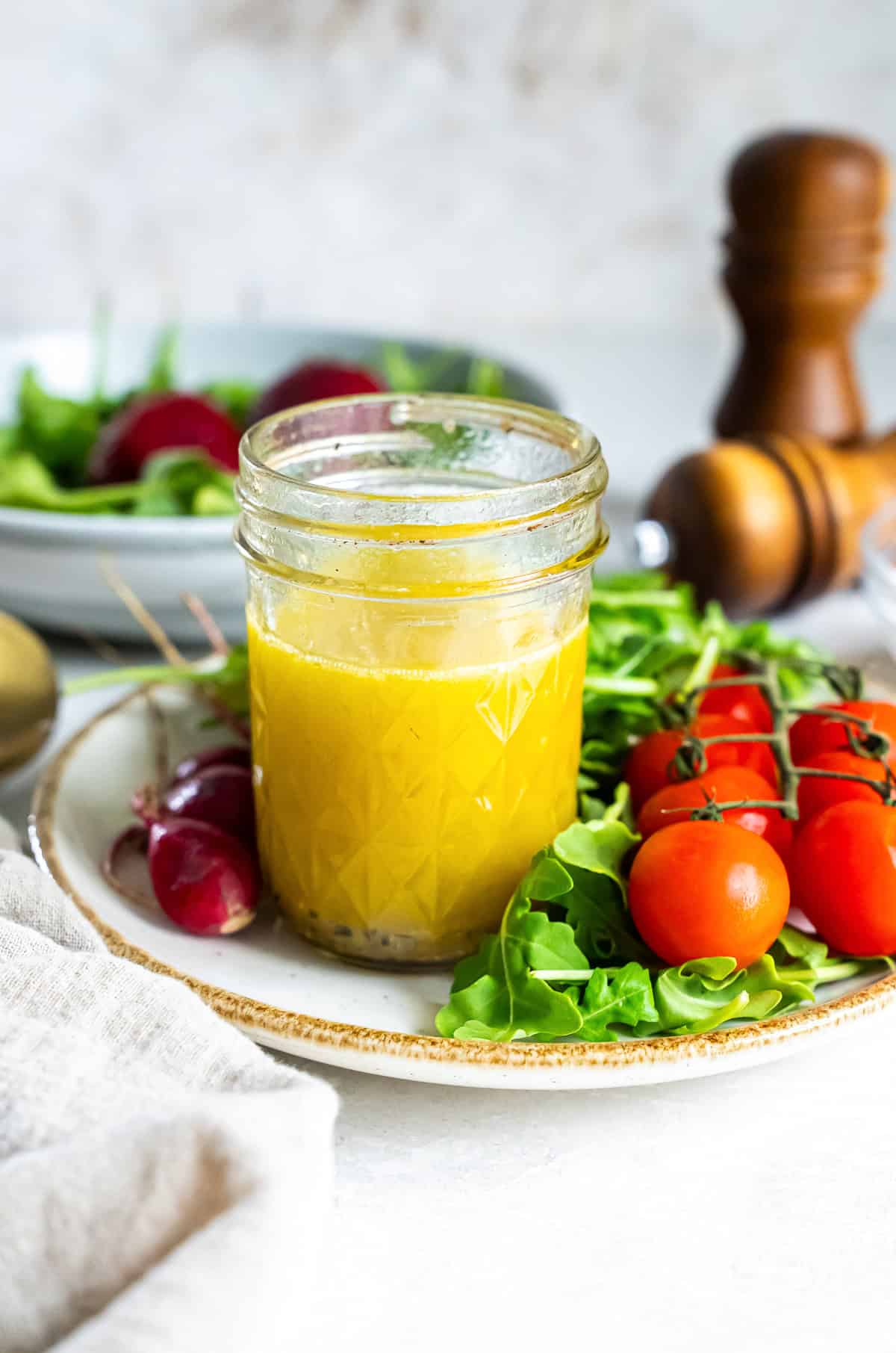 A mason jar filled with champagne vinaigrette on a plate with salad greens and cherry tomatoes.
