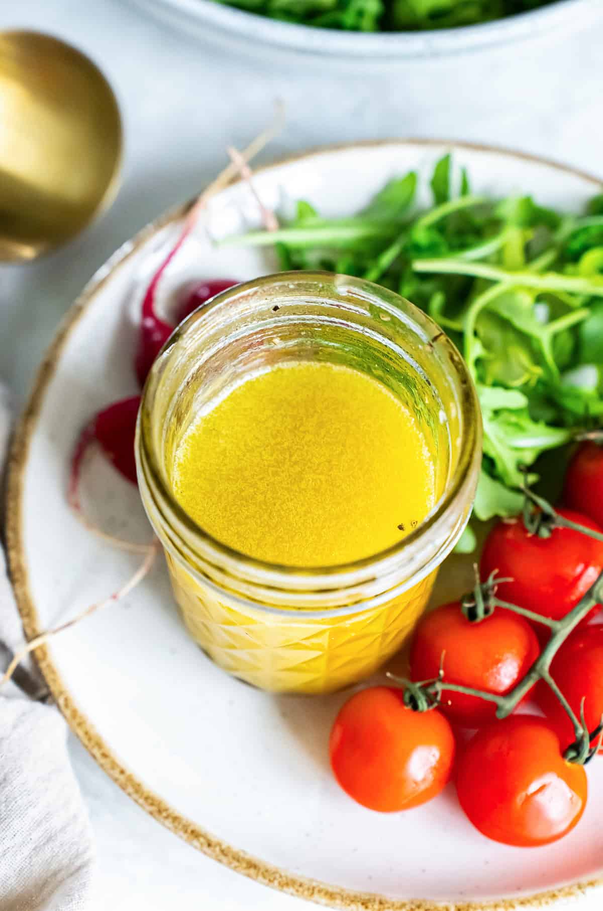Champagne vinaigrette in a mason jar resting on a plate with salad greens and cherry tomatoes.