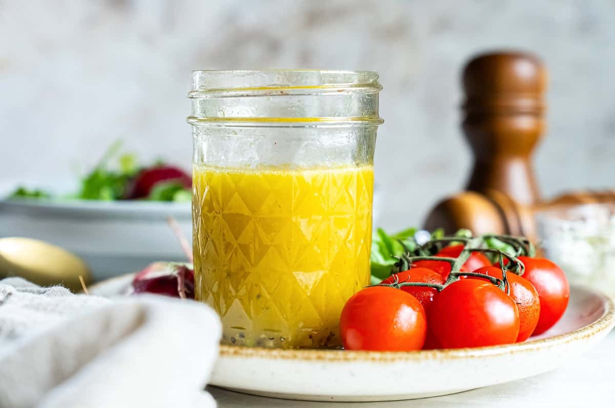 Champagne vinaigrette in a mason jar on a plate with cherry tomatoes.