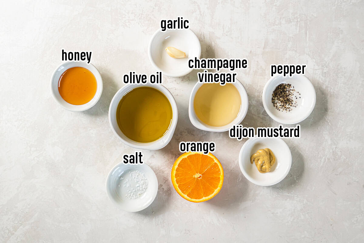 Champagne vinegar, olive oil, half of an orange and other ingredients in small bowls with text overlay.