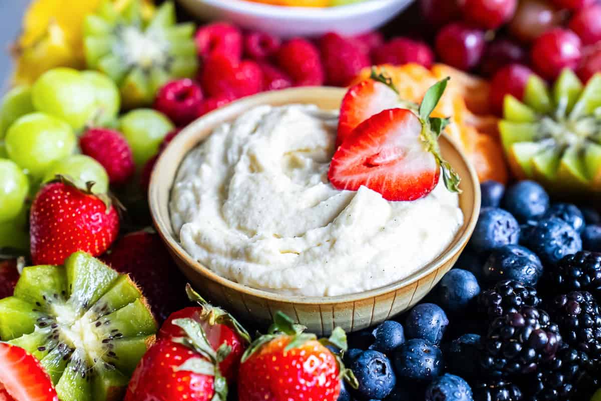 Mascarpone fruit dip topped with sliced strawberries on a fruit tray platter.