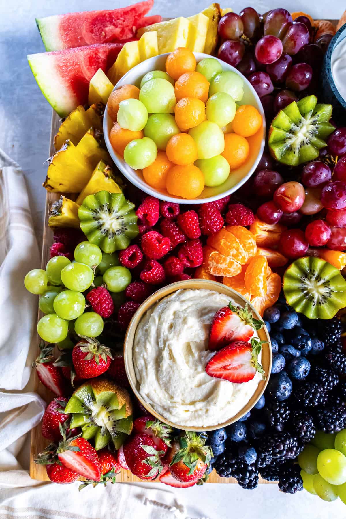 A fruit platter with melon balls, berries, grapes and kiwi with two bowls of fruit dip.