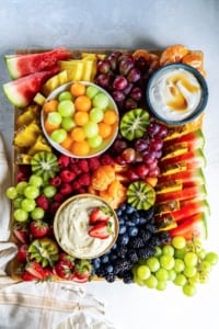 A fruit platter with melon balls, grapes, and other fruit and two fruit dips.