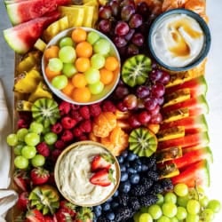A fruit platter with melon balls, grapes, and other fruit and two fruit dips.