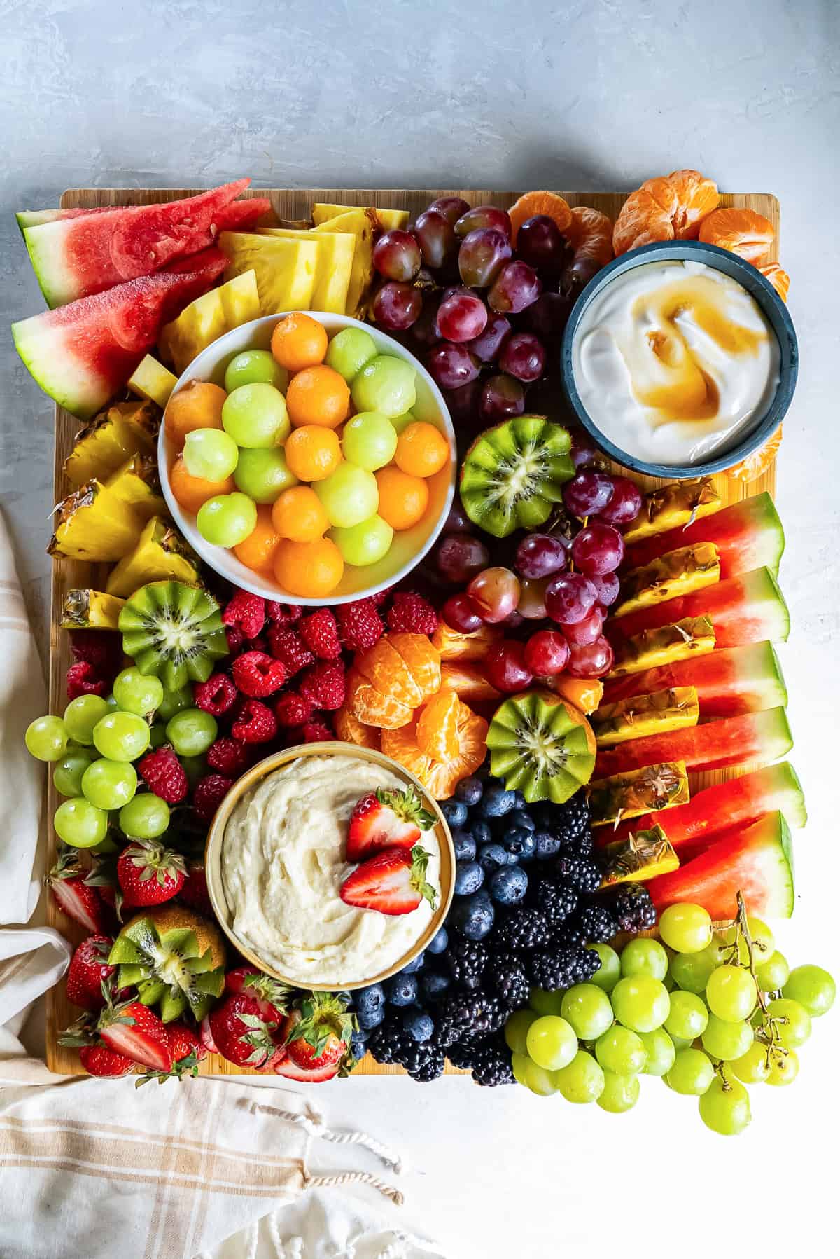 A fruit platter with melon balls, grapes, and other fruit and two fruit dips.
