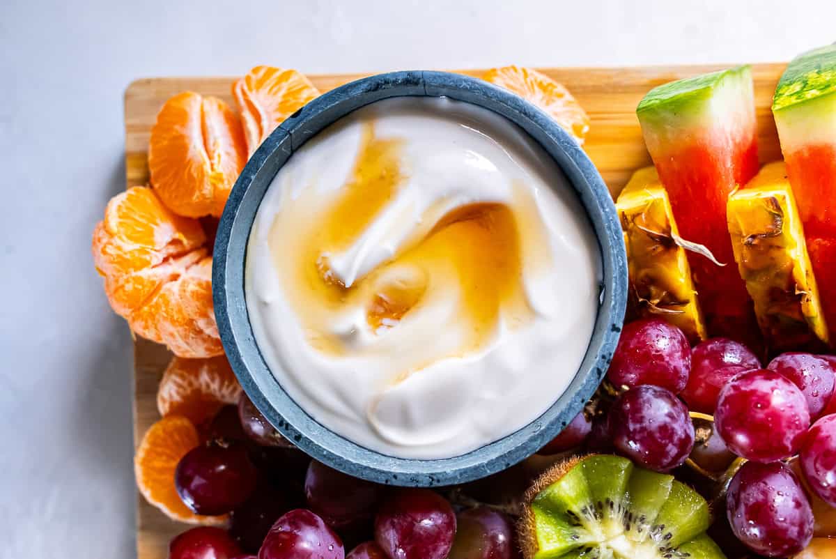 Greek yogurt fruit dip in a bowl topped with honey on a fruit platter.