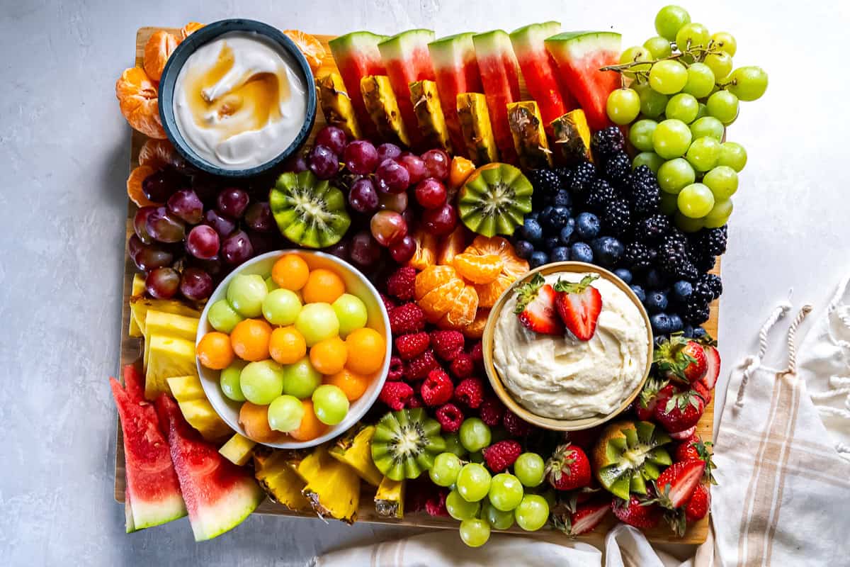 A fruit platter with melon, berries, grapes, and kiwi and two bowls of fruit dip.