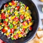 Mango cucumber salsa in a black serving bowl with tortilla chips scattered around it.