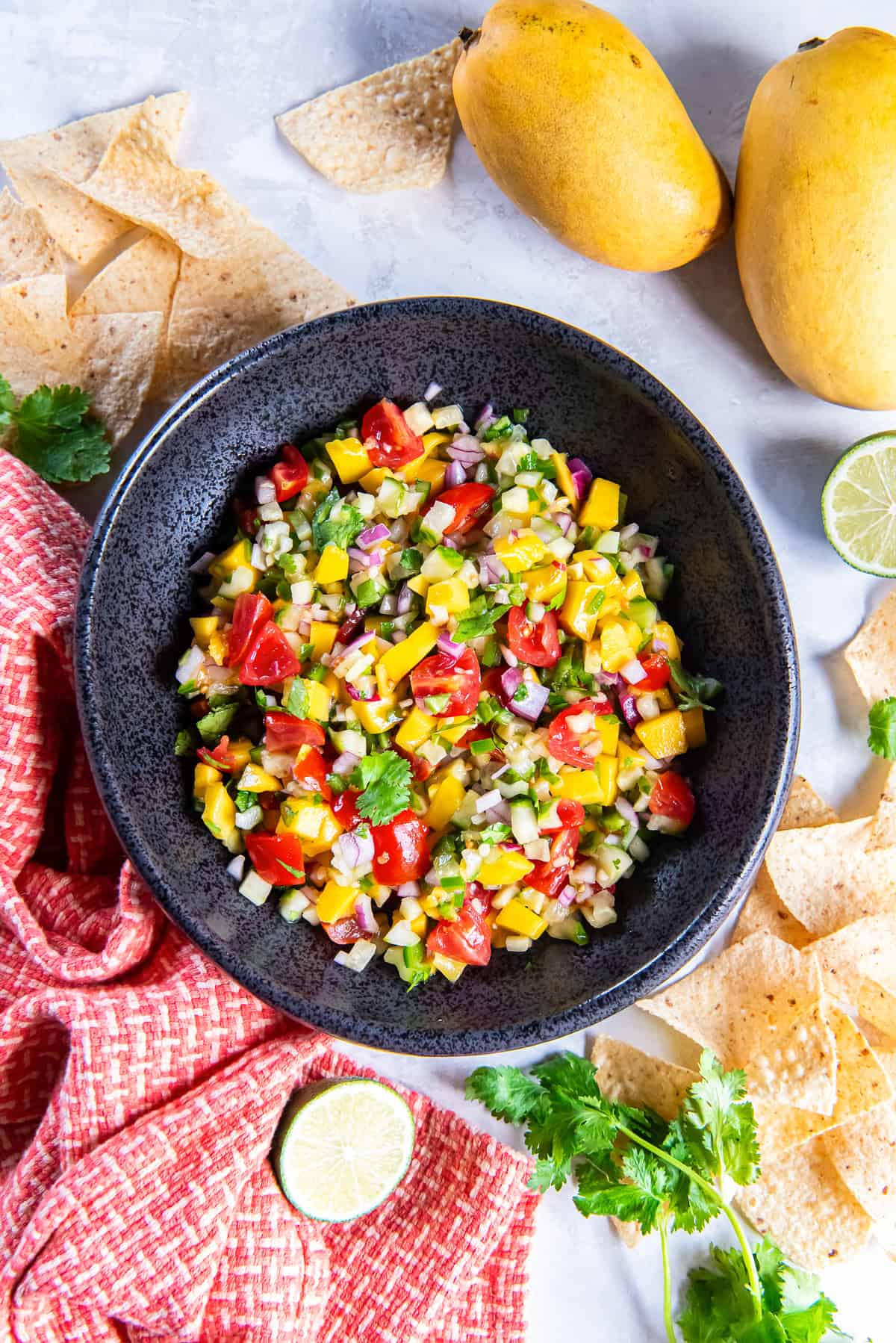 A black bowl filled with mango cucumber salsa next to a kitchen cloth and tortilla chips.