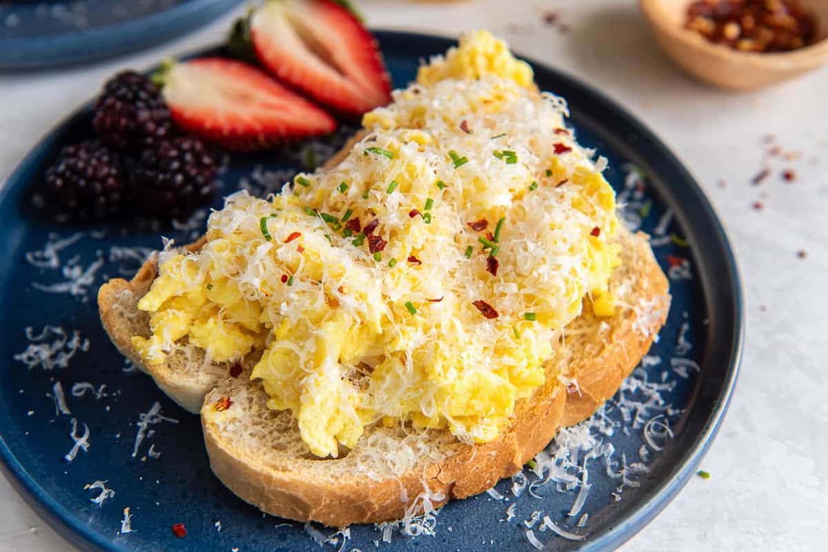 A slice of toast topped with ricotta scrambled eggs on a blue plate with berries.