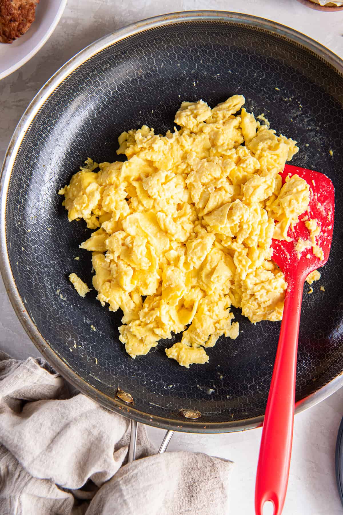 A red spatula resting in a skillet with ricotta scrambled eggs.