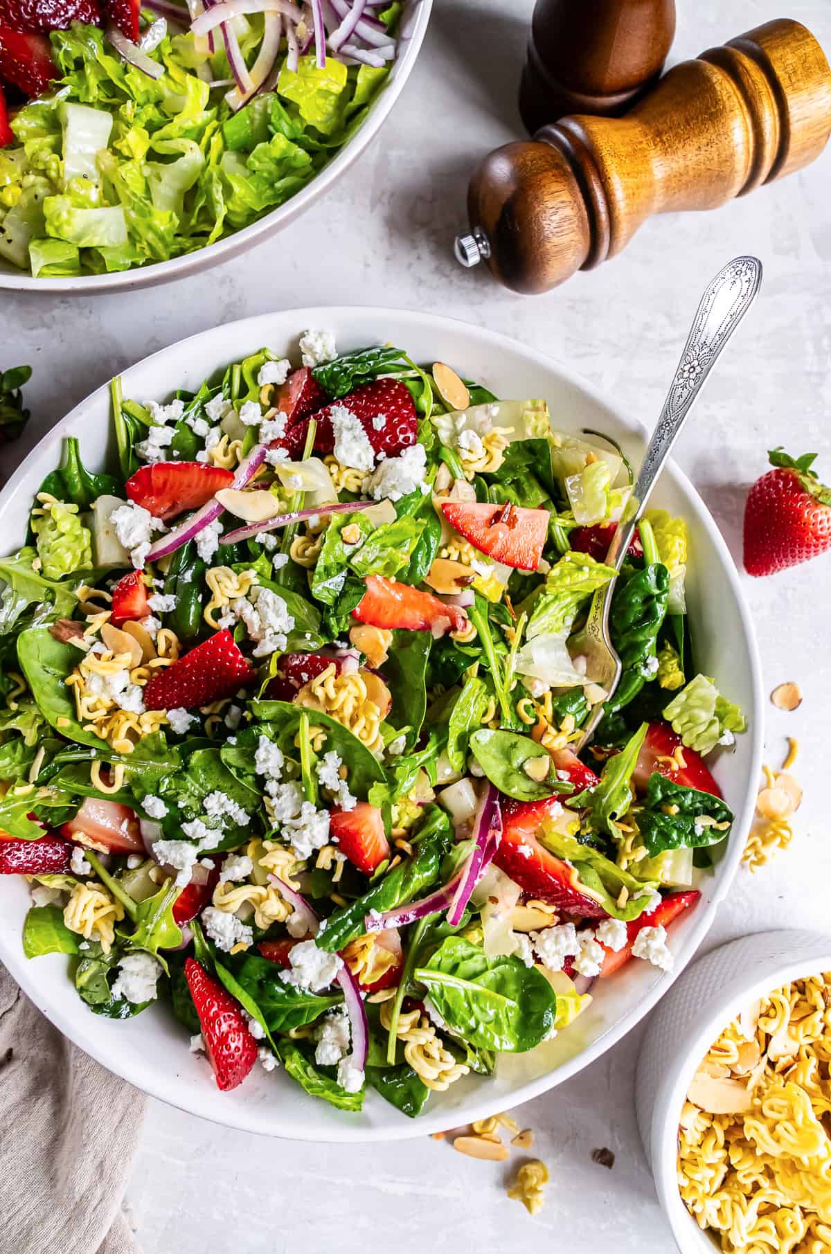 A fork resting in a bowl of strawberry crunch salad with greens, ramen noodles and champagne vinaigrette.