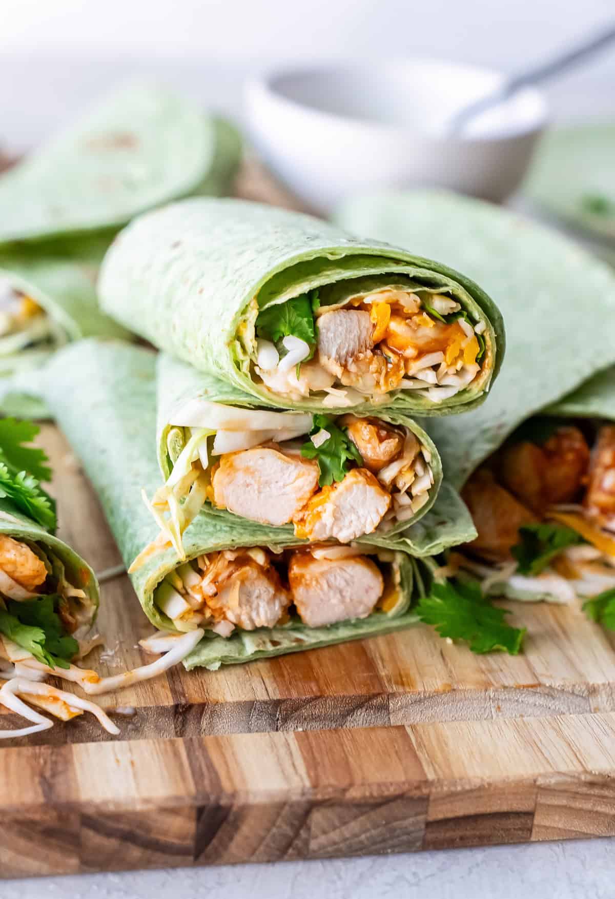 Halved bbq chicken wraps in green spinach tortillas stacked on a cutting board.