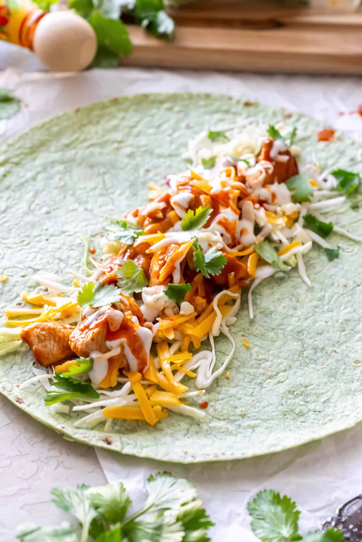 A spinach tortilla layered with bbq chicken, shredded cabbage, cheese, cilantro, and Ranch dressing.