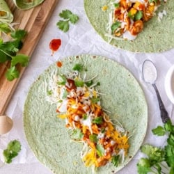 Two open face BBQ chicken wraps next to a cutting board filled with rolled wraps.