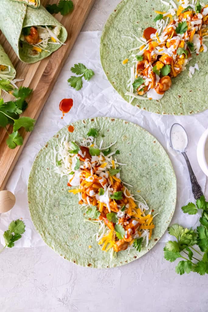 Two open face BBQ chicken wraps next to a cutting board filled with rolled wraps.