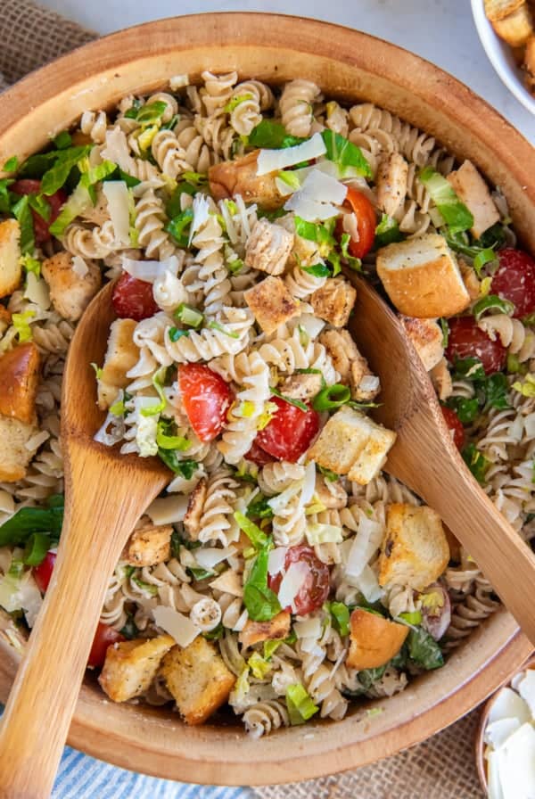 Salad spoons resting in a bowl of chicken caesar pasta salad.