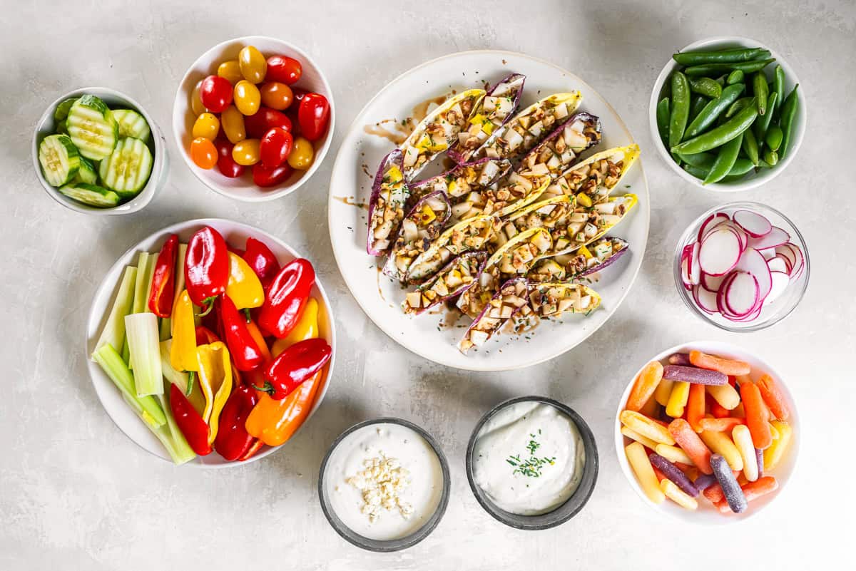 Mini bell peppers, cucumber slices and other crudite platter ingredients and dips in bowls with text overlay