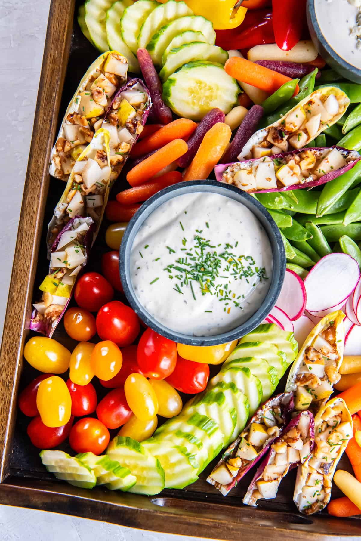 Assorted vegetables on a wood board with two bowls filled with creamy dips.
