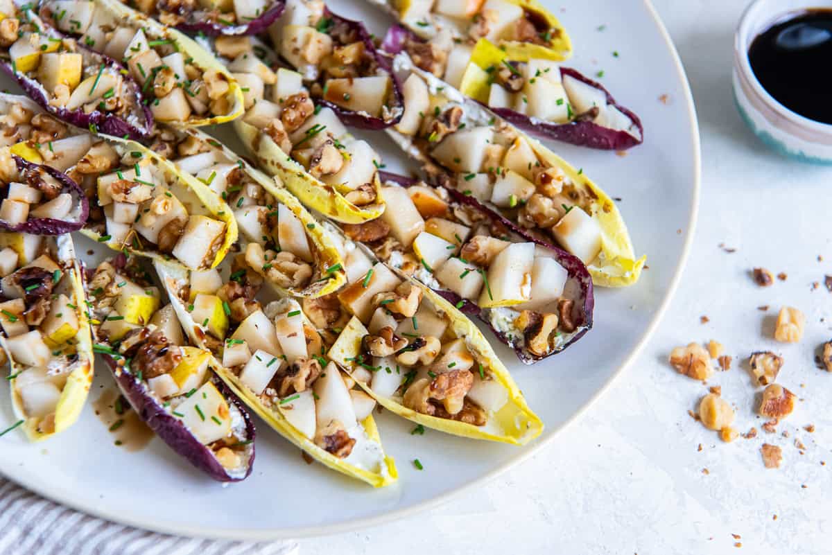 Endive Appetizer with Goat Cheese and Pear 4 Belgian endive leaves stuffed with goat cheese, pear, and walnuts on a white plate.