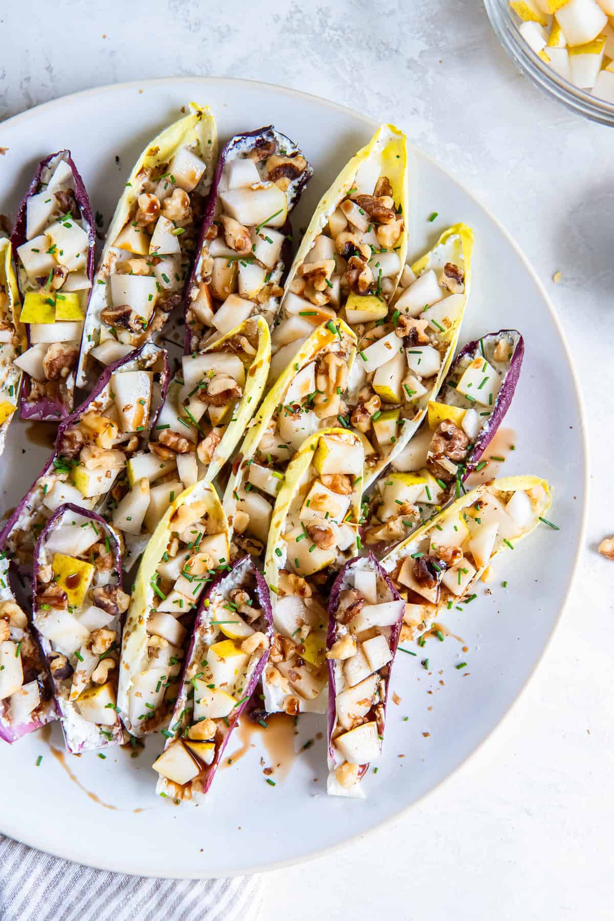 Endive Appetizer with Goat Cheese and Pear 6 Goat cheese and walnut stuffed endive with balsamic glaze on a white plate.