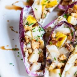 Endive Appetizer with Goat Cheese and Pear 7 Stuffed endive with balsamic glaze on a white plate.