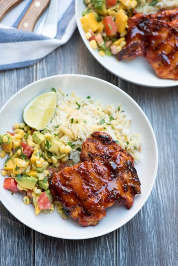 Grilled chipotle maple chicken in white bowls with rice and mango salsa.