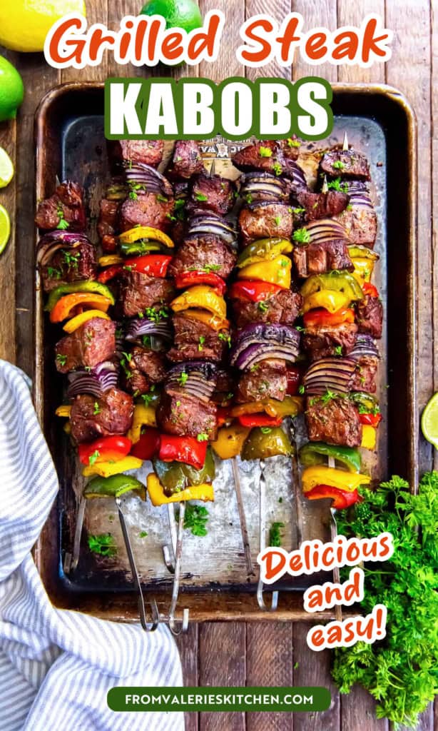 Grilled steak kabobs with peppers and onions on a baking sheet surrounded my lemons and limes with text overlay.