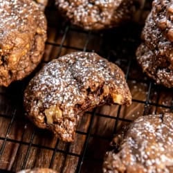 Chocolate Oatmeal Cookies 8 Chocolate oatmeal cookies dusted with powdered sugar on a wire rack with a bite missing from the one in the center.