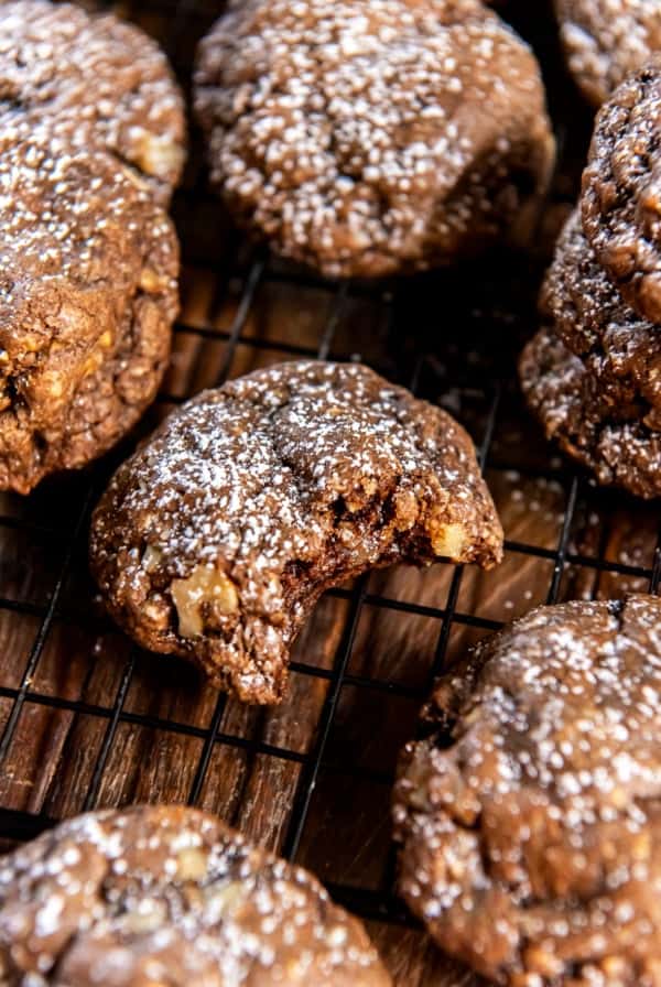 Chocolate oatmeal cookies dusted with powdered sugar on a wire rack with a bite missing from the one in the center.