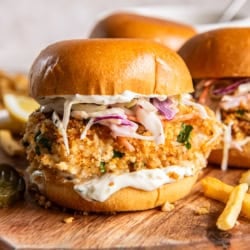 Fish sandwiches with coleslaw on a wood board with French fries.