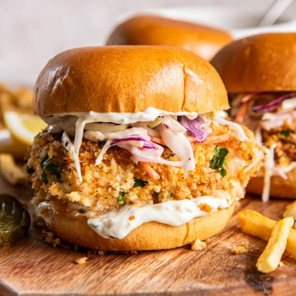 Fish sandwiches with coleslaw on a wood board with French fries.