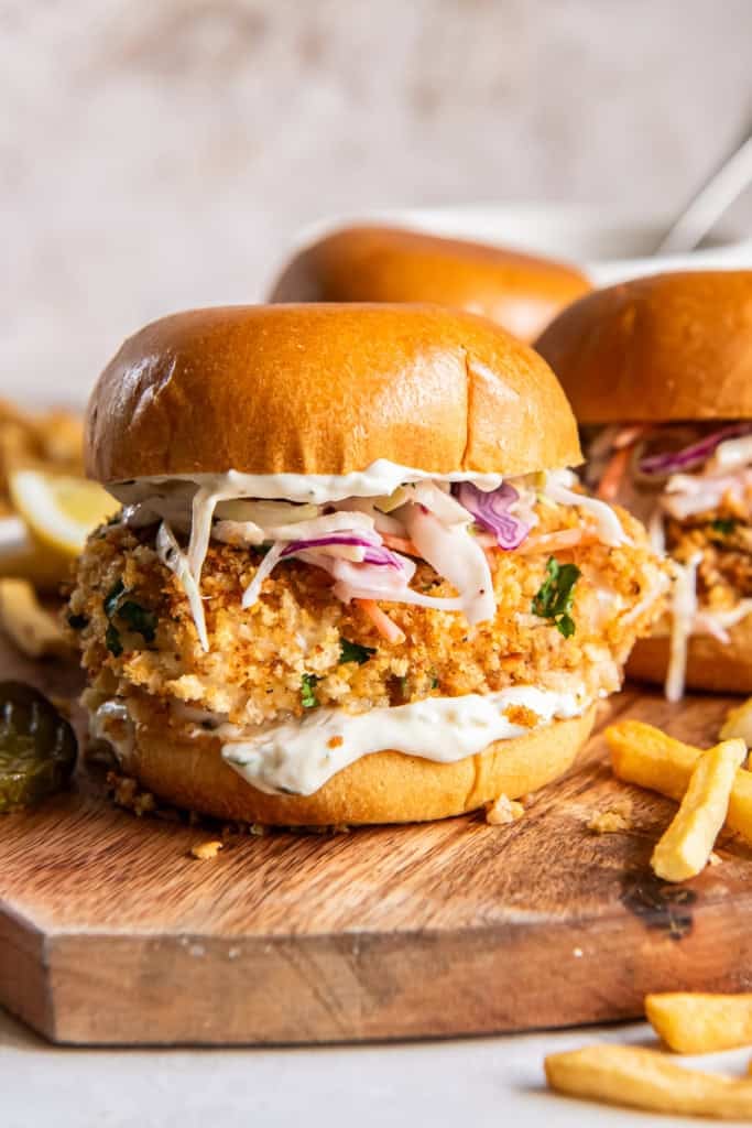 Fish sandwiches with coleslaw on a wood board with French fries.