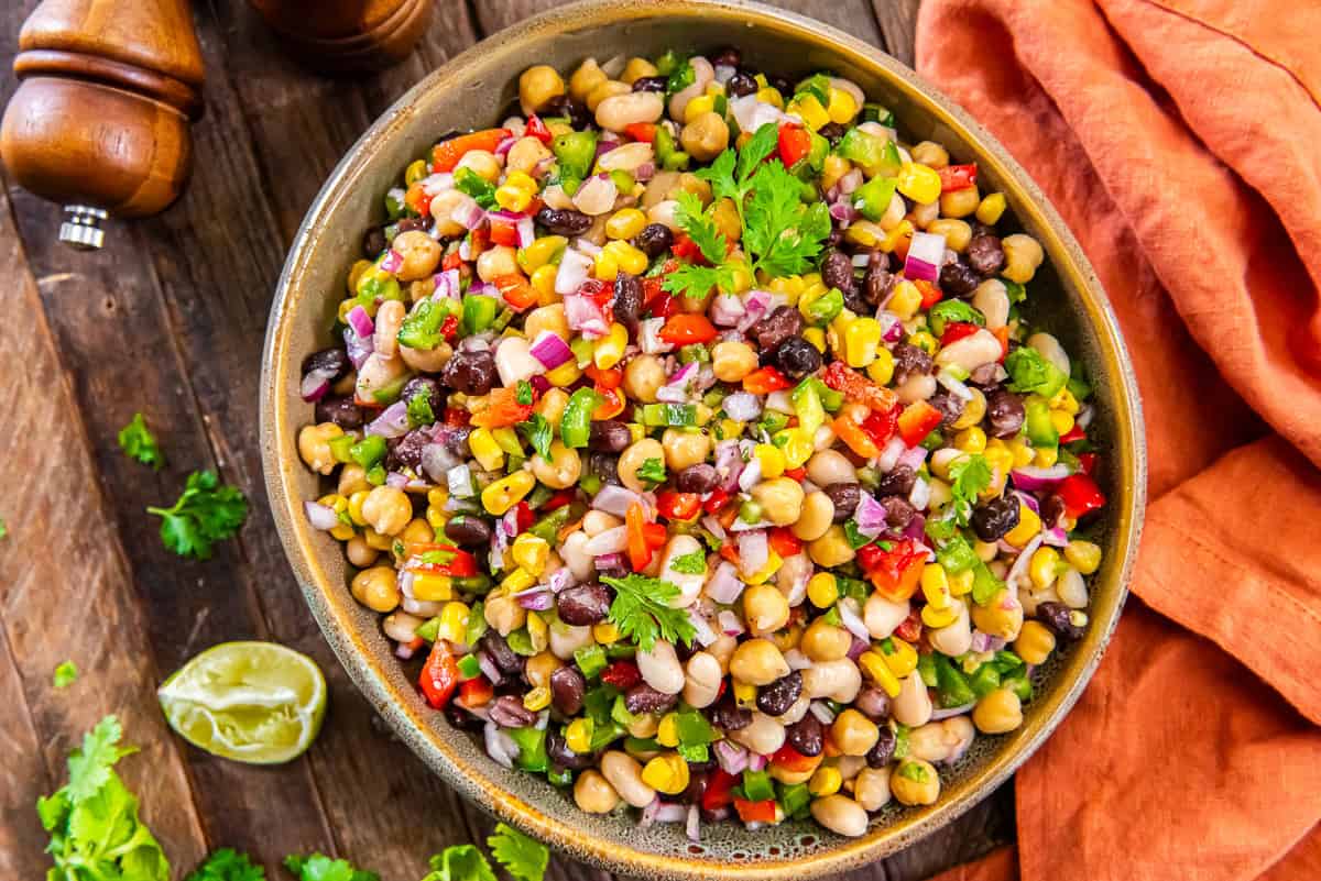Mexican Bean Salad 4 Mexican bean salad with black beans, white beans, chickpeas, and corn in a wood bowl next to lime wedges.