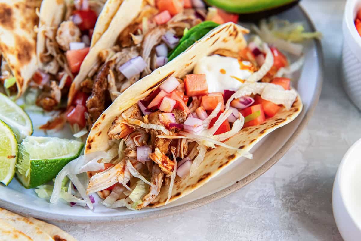 Chicken tacos on a paltter with half an avocado.