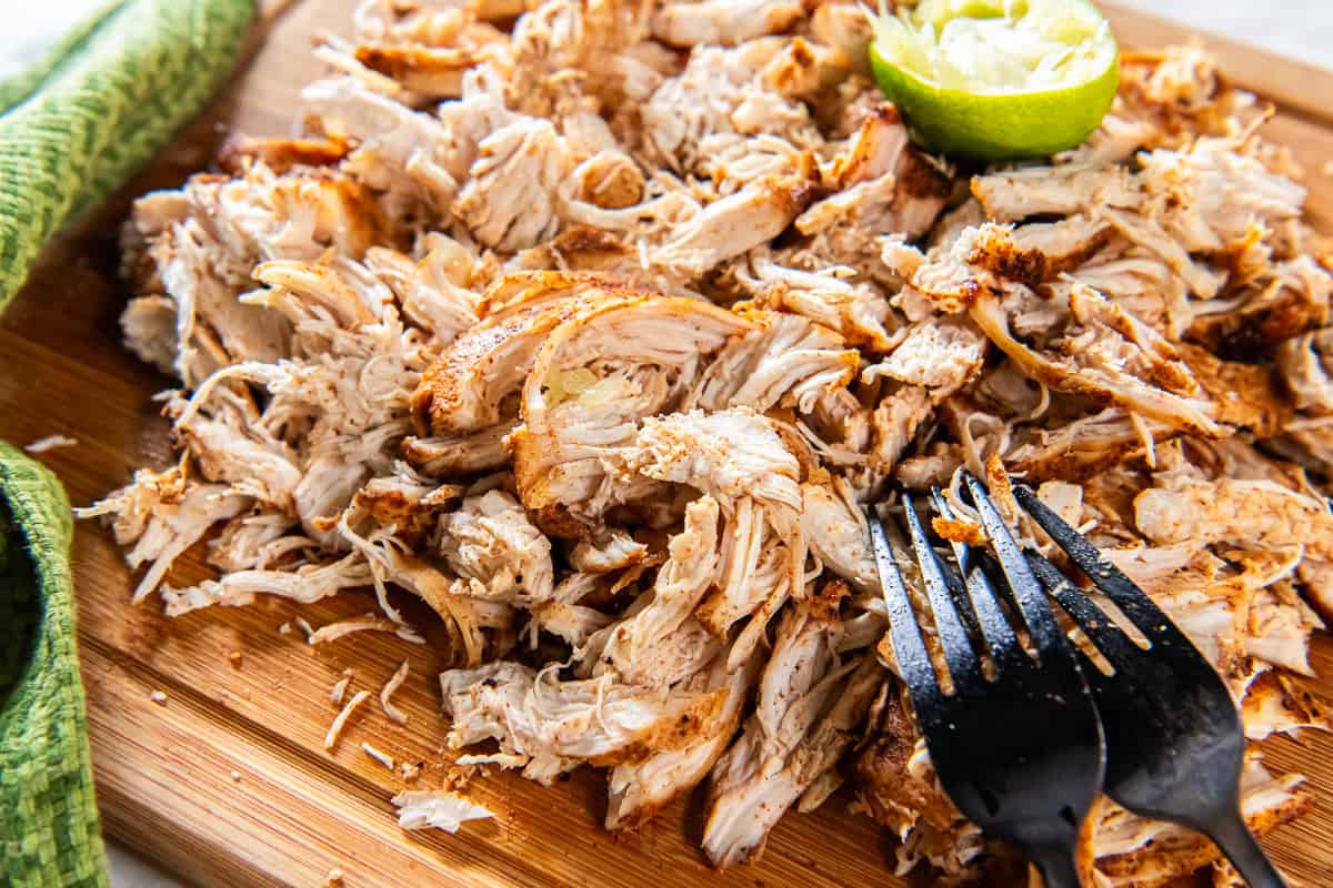 Mexican shredded chicken on a cutting board with two forks.