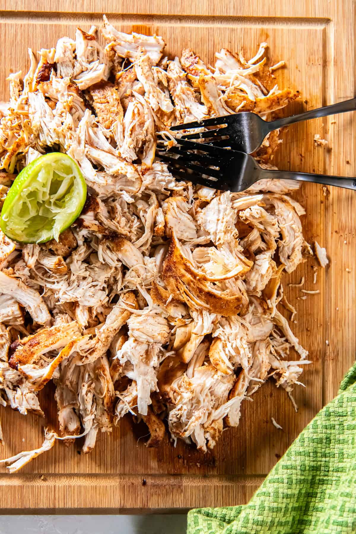 Mexican shredded chicken on a cutting board with forks and a spent lime.