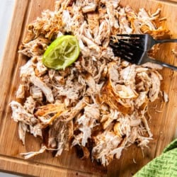 Mexican shredded chicken on a cutting board with forks and a spent lime.