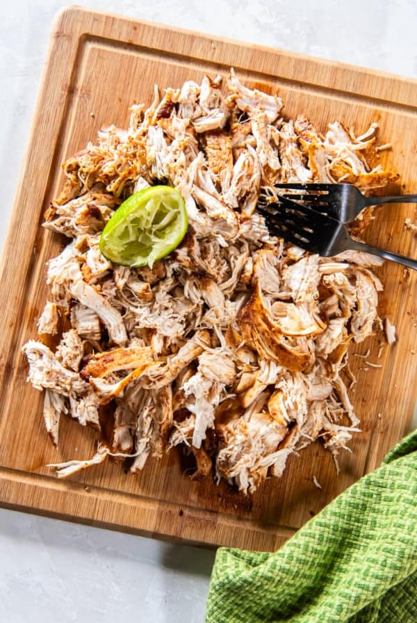 Mexican shredded chicken on a cutting board with forks and a spent lime.
