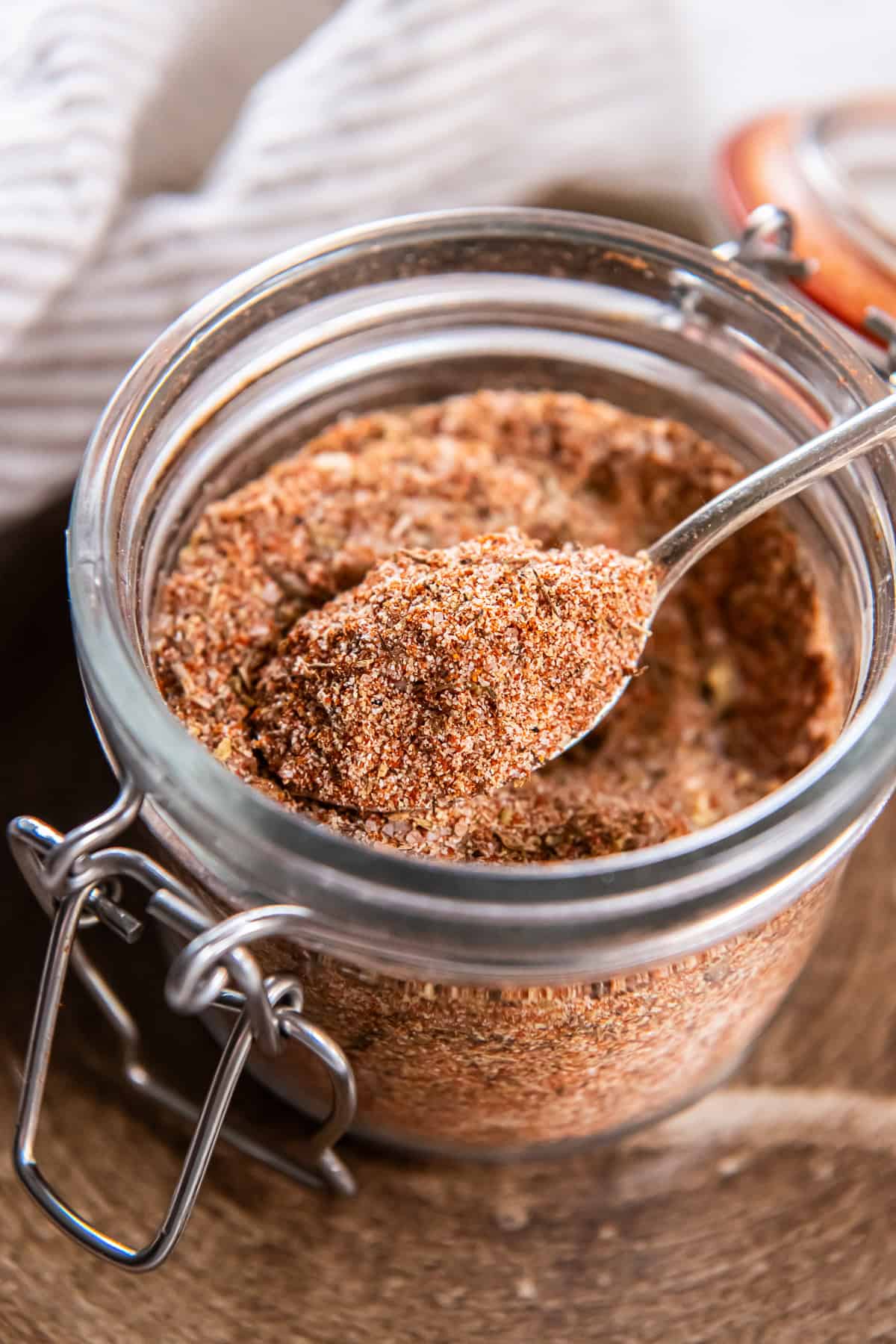 Spoon scooping homemade Cajun seasoning mix from a glass jar.