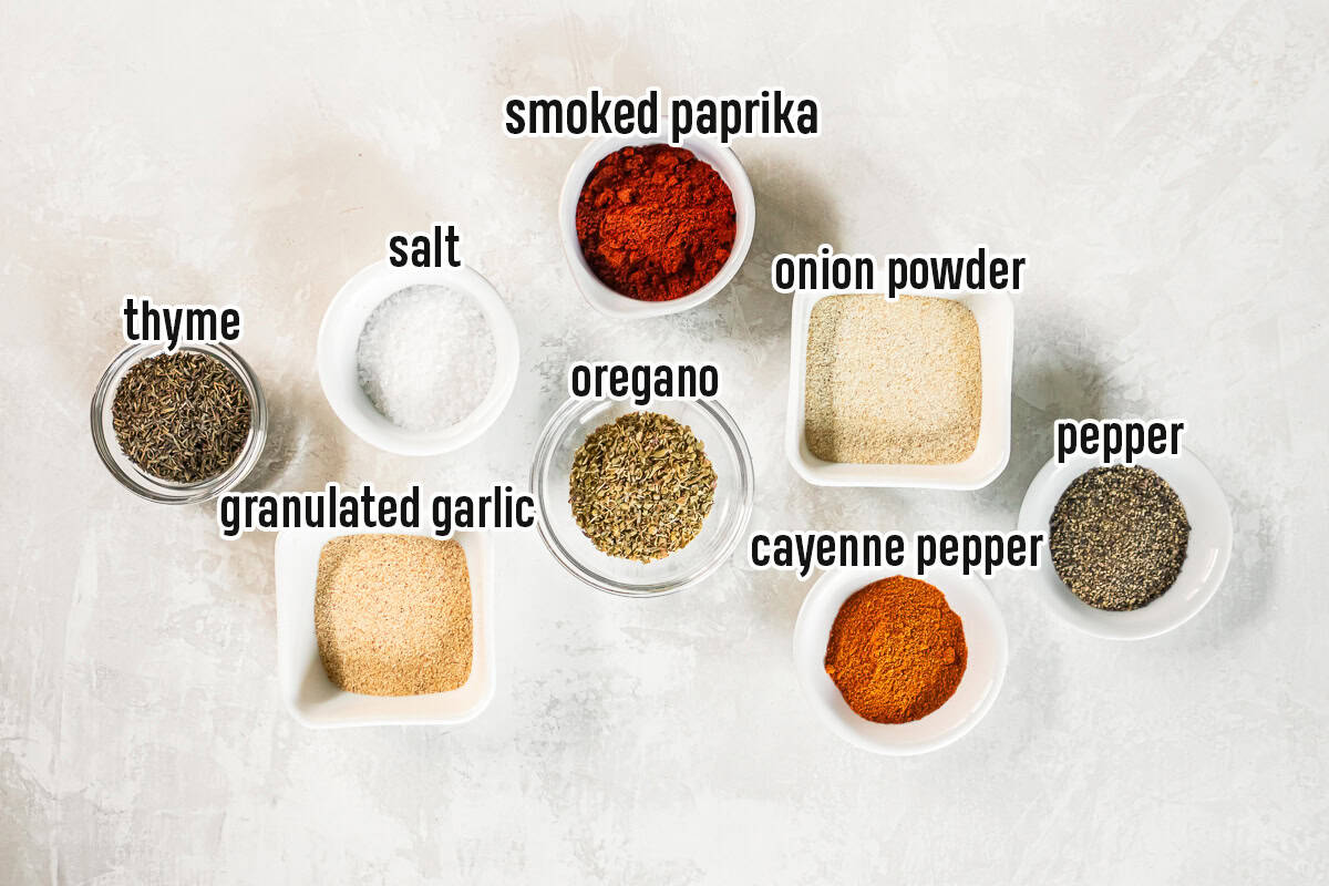 Smoked paprika, oregano, and other dried spices for Cajun seasoning in small bowls with text overlay