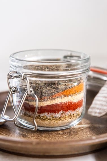 Glass jar filled with layered spices for homemade Cajun seasoning mix.