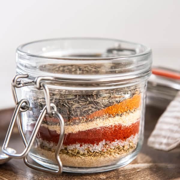 Glass jar filled with layered spices for homemade Cajun seasoning mix.