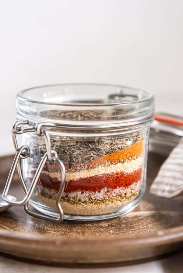 Glass jar filled with layered spices for homemade Cajun seasoning mix.