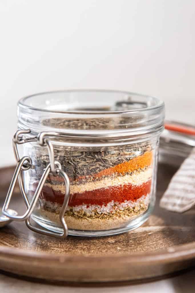 Glass jar filled with layered spices for homemade Cajun seasoning mix.