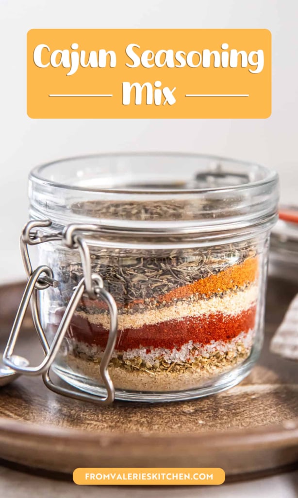 Glass jar filled with layered spices for homemade Cajun seasoning mix with text overlay.